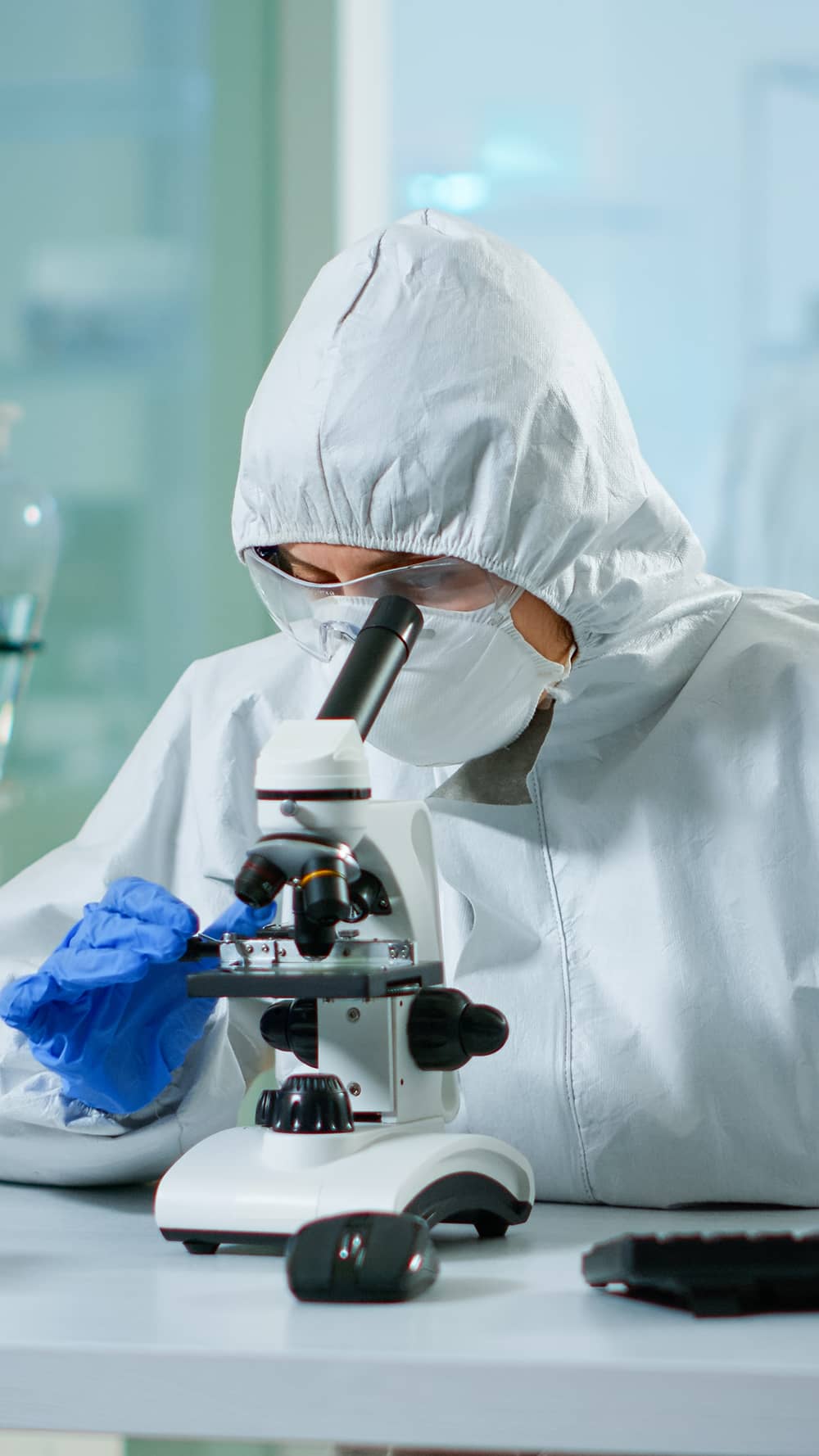 biologist-doctor-coverall-checking-dna-sample-microscope-typing-pc-equipped-lab-examining-vaccine-evolution-medical-lab-using-high-tech-chemistry-tools-scientific-research